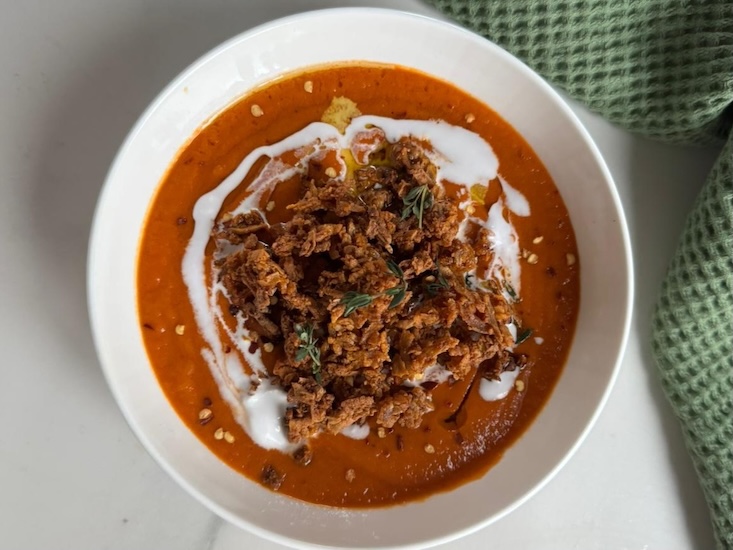 מרק עגבניות, בזילוף שמן זית וקרם קוקוס, וקרוטוני טופו קריספיים מעל.