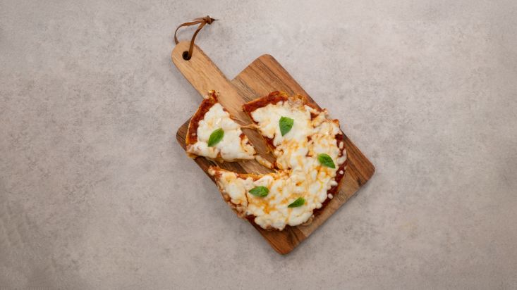 פיצה טופו מוכנה, על קרש הגשה ופיזור בזיליקום מעל.