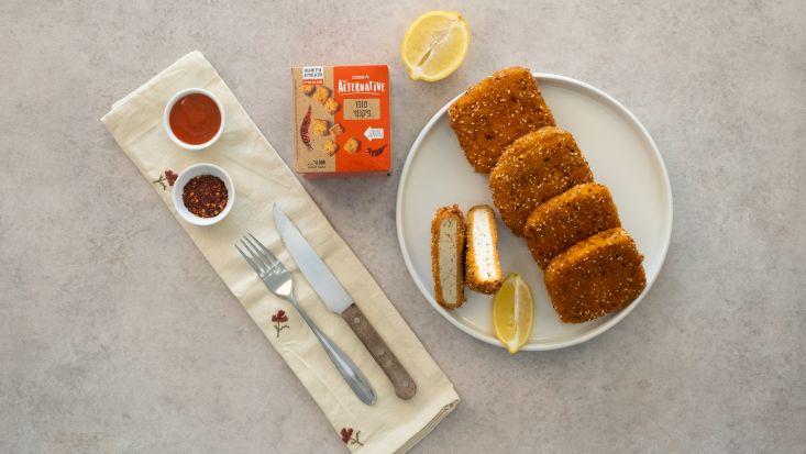 שניצל טופו פריך בצלחת הגשה, לצד חבילת טופו פיקנטי, לימון ורטבים