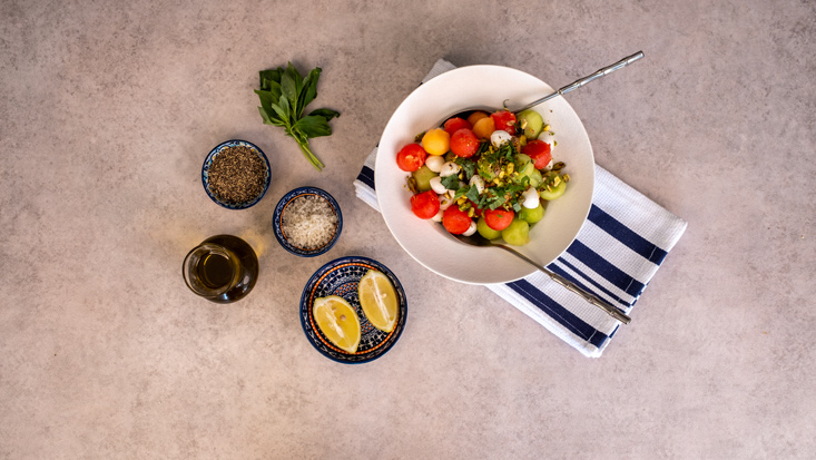 סלט מלון ואבטיח עם בייבי מוצרלה, מוגש לצד פלחי לימון ותבלינים.