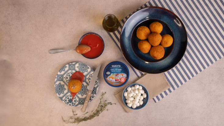 ארנציני פתיתים במילוי בייבי מוצרלה, בצלחת הגשה עם רוטב עגבניות, לצד בייבי מוצרלה.