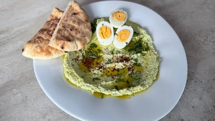 חומוס מפולי סויה בצלחת, ומעל ביצים קשות ופיתות.