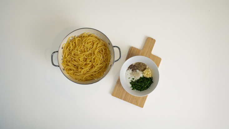 פסטה מבושלת במסננת, לצד מרכיבי הרוטב בקערה.